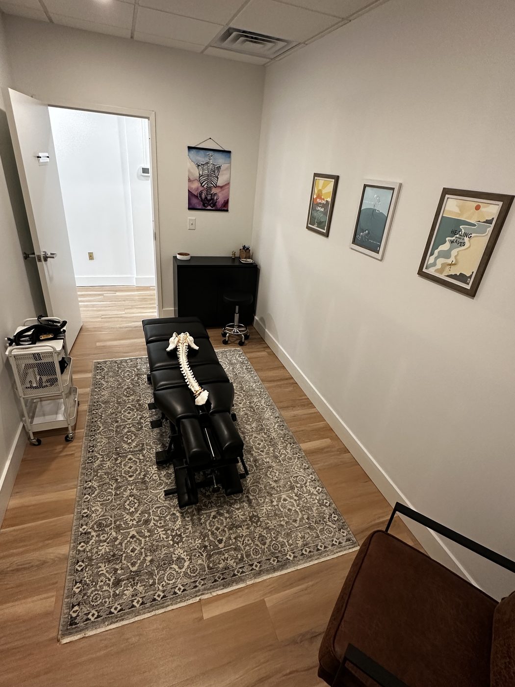 The adjusting room, with the adjusting table on a patterned rug, framed prints along the wall and a window at the far end