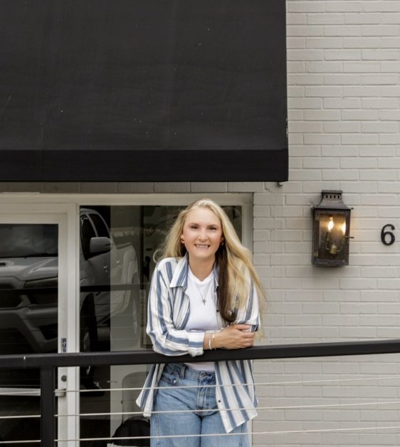 Dr. Shannon standing outside Common Grace Chiropractic & Wellness at 6 Sevier Street, leaning on the railing under the black awning, with the lantern and house number on the white brick beside her